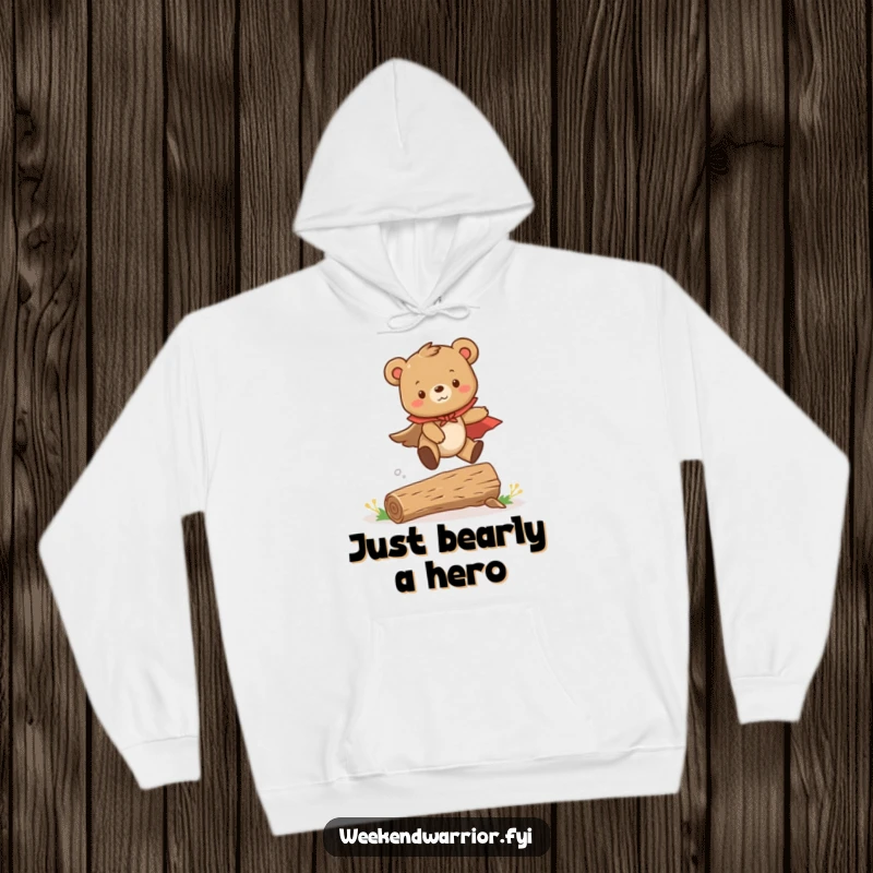 Funny hoodie depicting a cute bear cub in a cape, courageously leaping over a tiny log, offering warmth and heroic charm.